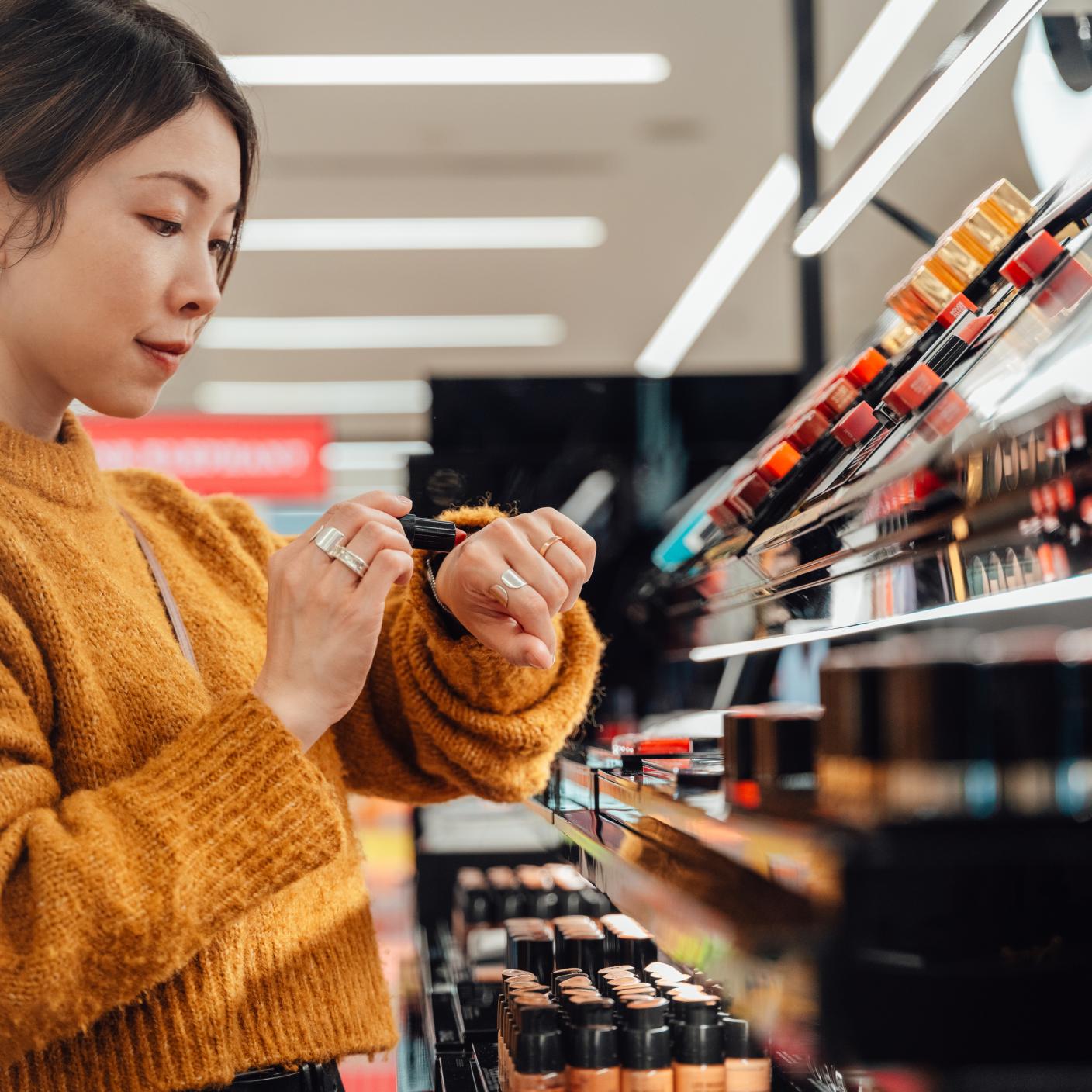 Young person picking lipstick shades at cosmetics counter.