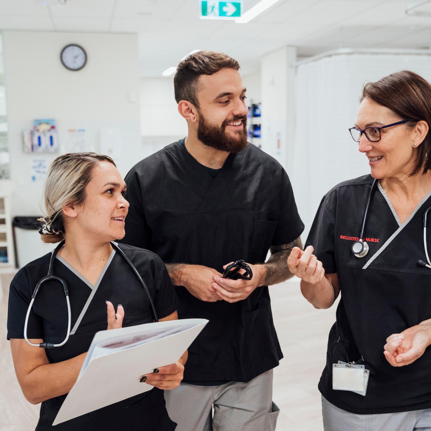 three healthcare workers walking and talking through the hospital ward.