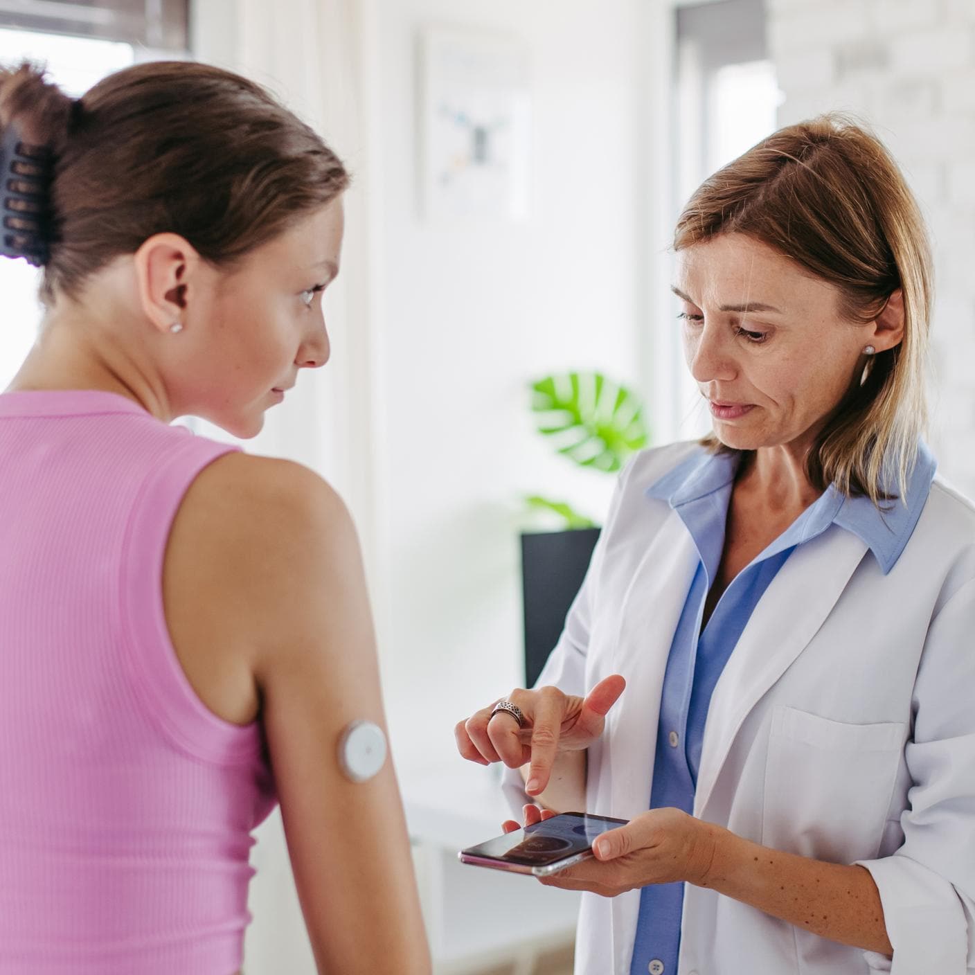 Diabetologe verbindet das Smartphone mit dem kontinuierlichen Blutzuckermessgerät am Arm des jugendlichen Patienten