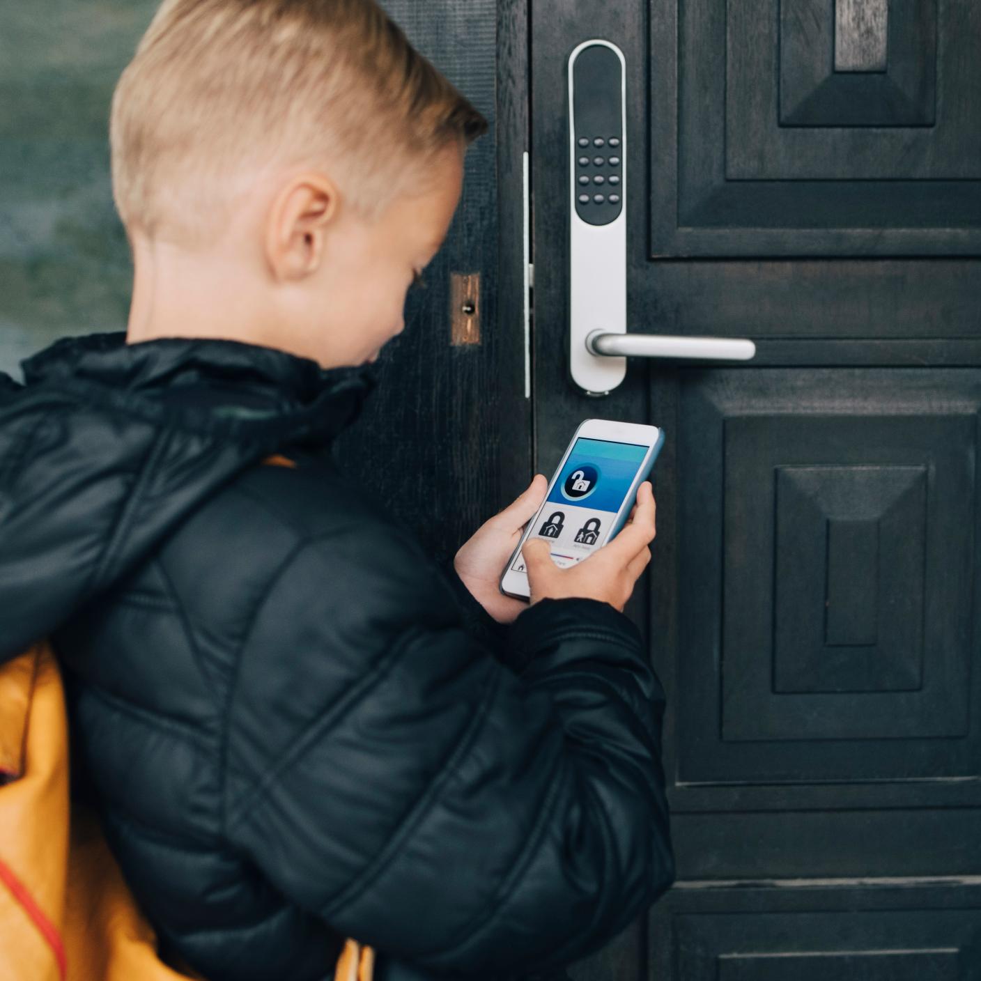 Rear view of boy using app on smart phone to unlock house door.