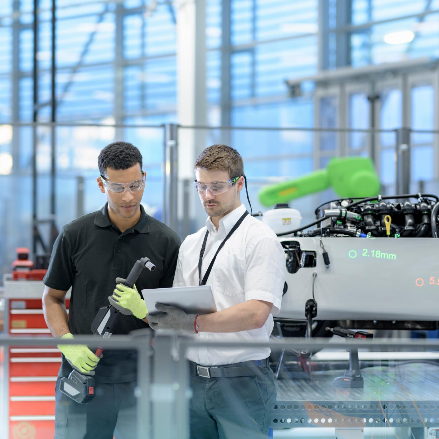 Engineers with digital tablet and robot inspecting car in robotics research facility.