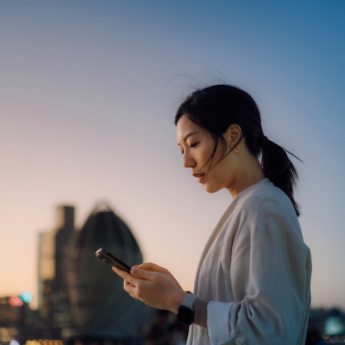 Moderne junge Frau, die unterwegs in der Stadt Textnachrichten auf dem Smartphone schreibt.