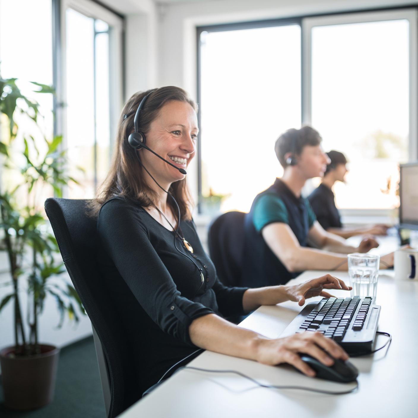 Une représentante souriante du service à la clientèle portant un casque d’écoute et utilisant un ordinateur dans un bureau