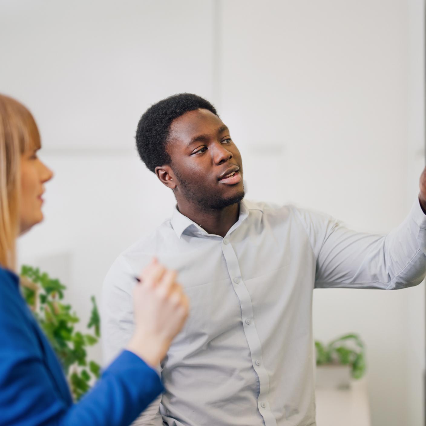 Two professionals engaged in a discussion in a meeting room, with one person pointing to information being reviewed.