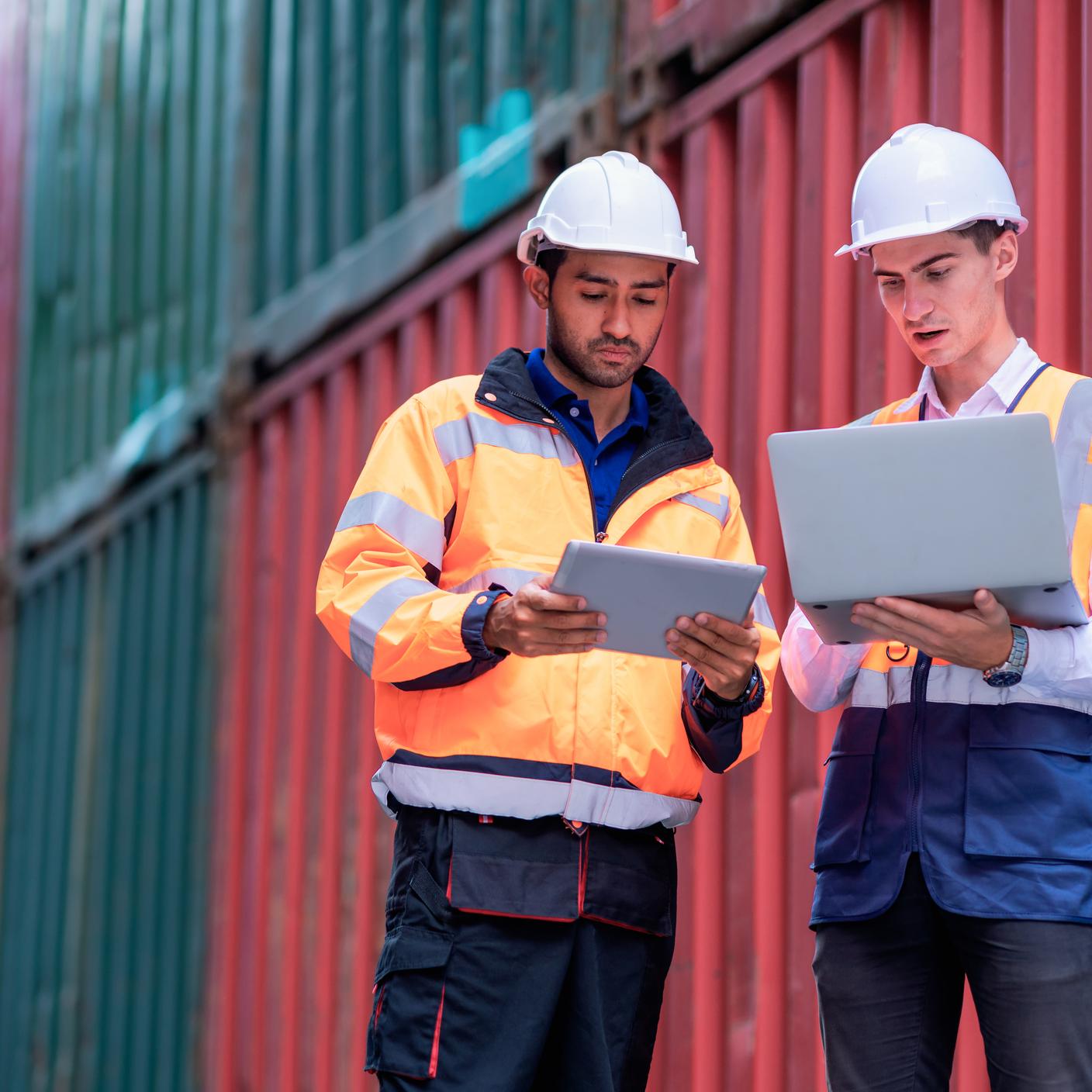 Supply Chain - Male Dock worker holding a tablet computer and explaining to a supervisor