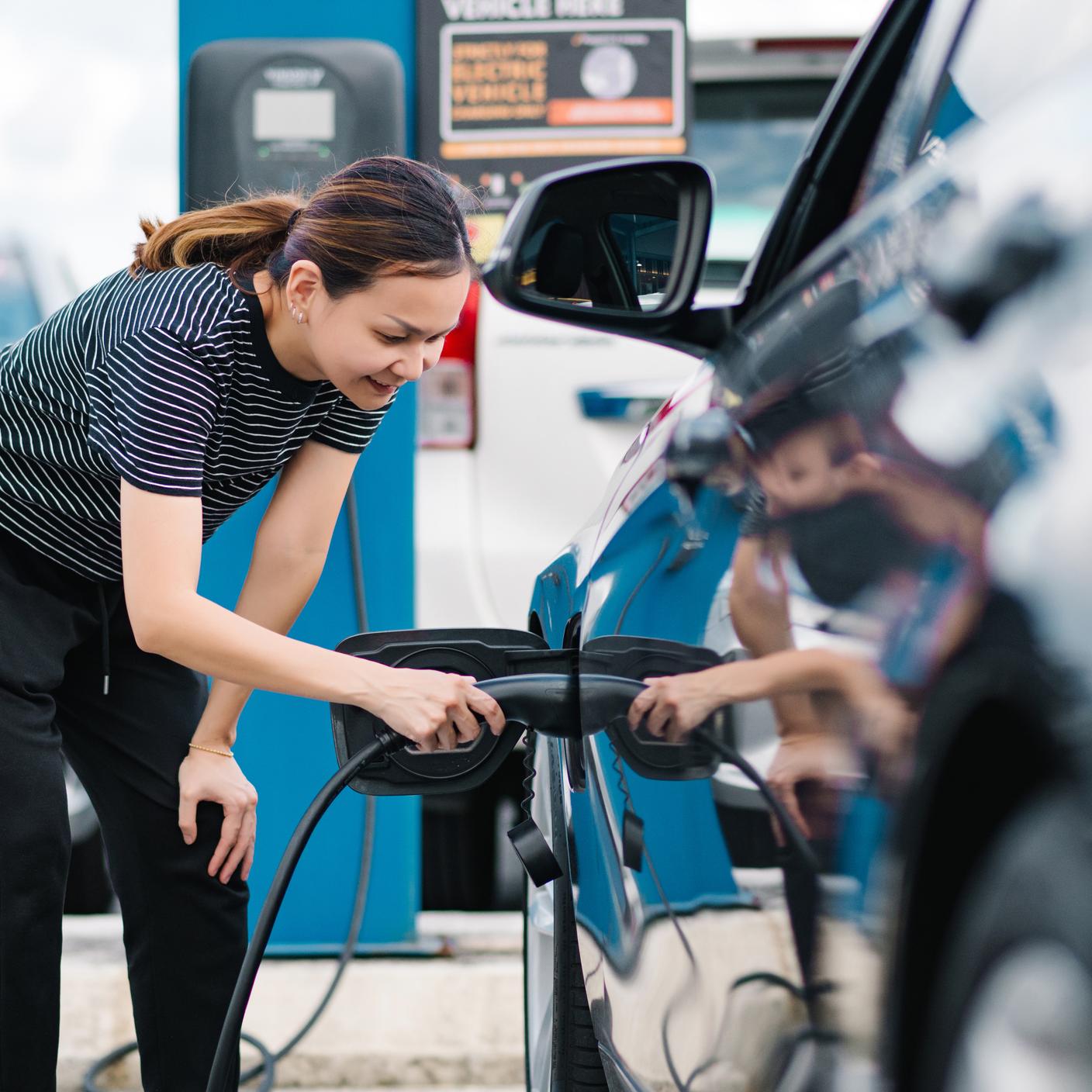 Asiatisches Mädchen lädt Elektroauto