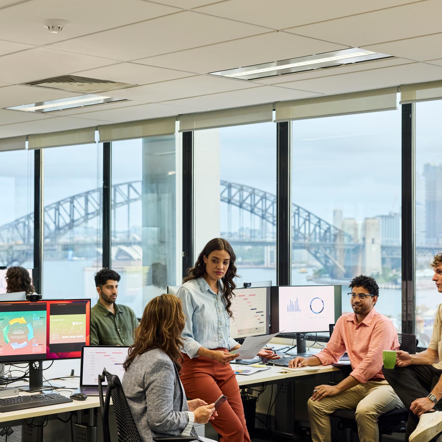 Female entrepreneur listening to coworker in meeting at office. Business professionals sharing ideas at work space. City is seen through transparent window.