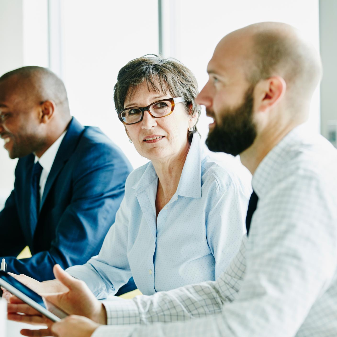 Smiling mature businesswoman listening during meeting with colleagues in office conference room