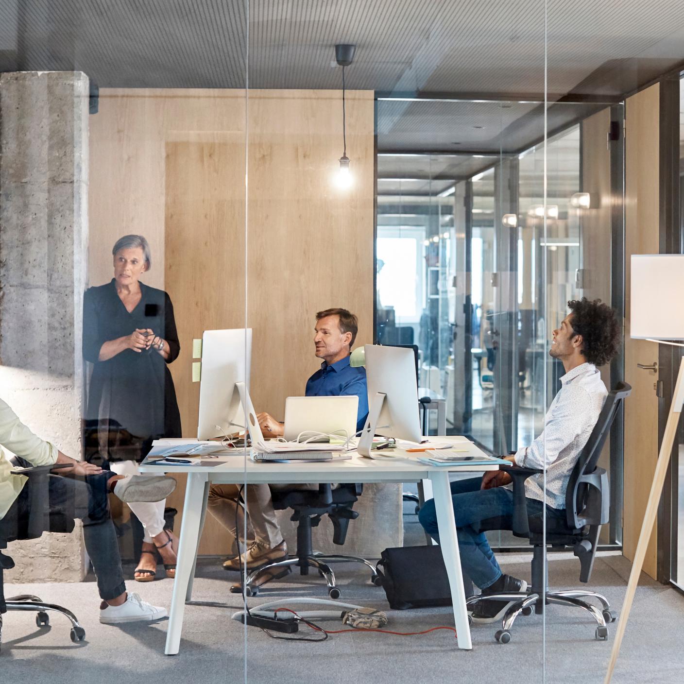 Multi-ethnic business people discussing in board room. Male and female professionals are working in new office. They are seen through glass.