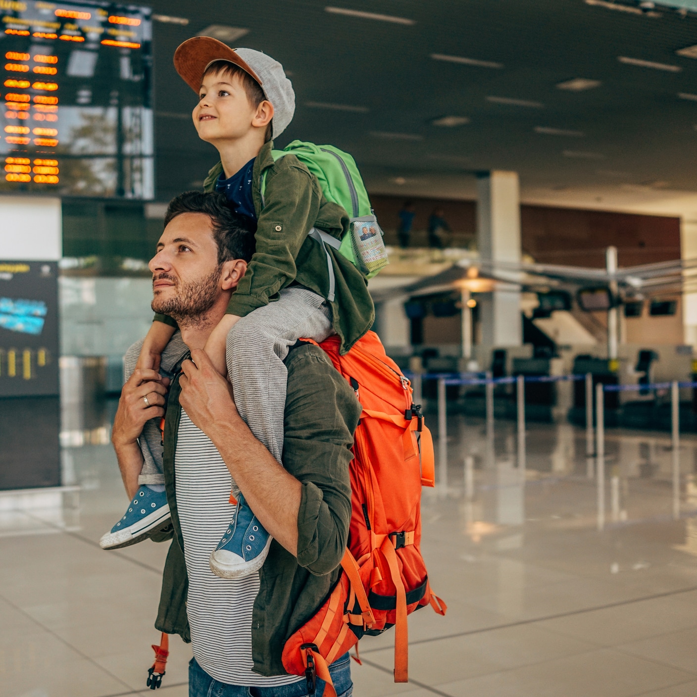 Photo of a cheerful little boy and his father, who travel together waiting for their flight at the airport.