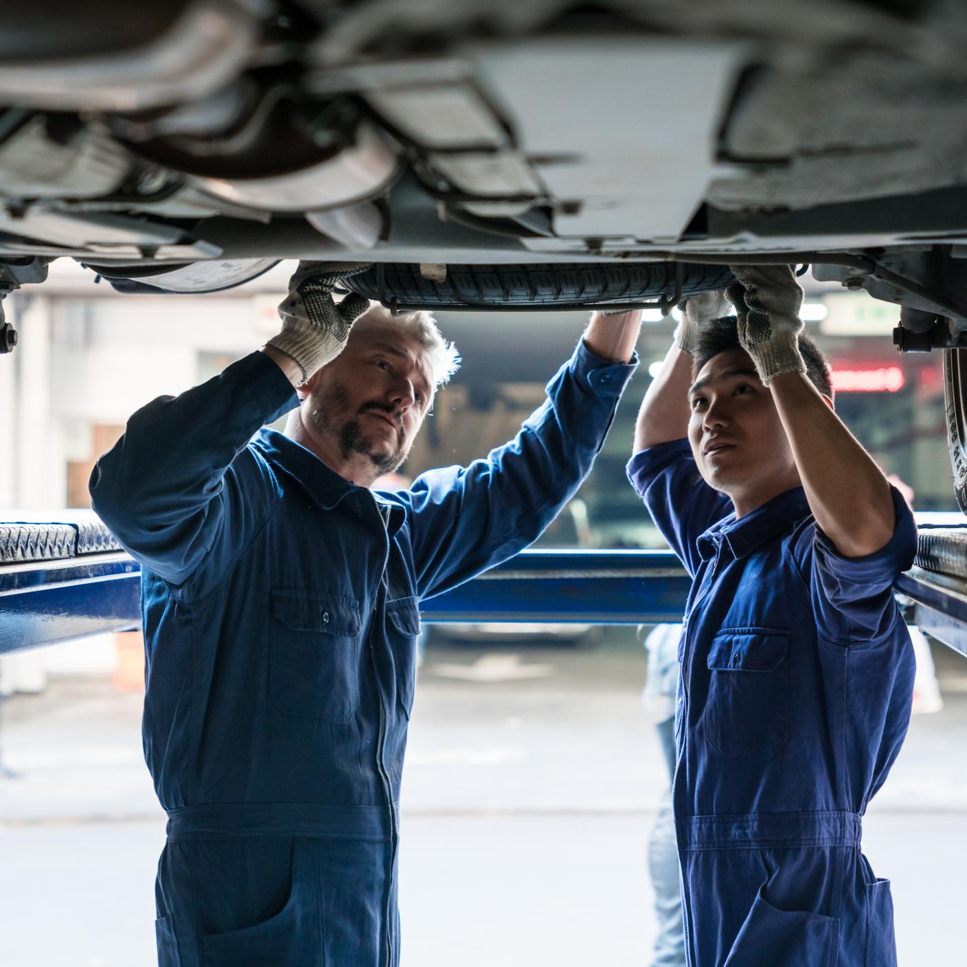 Mature auto mechanic and apprentice checking vehicle chassis in the auto repair shop.