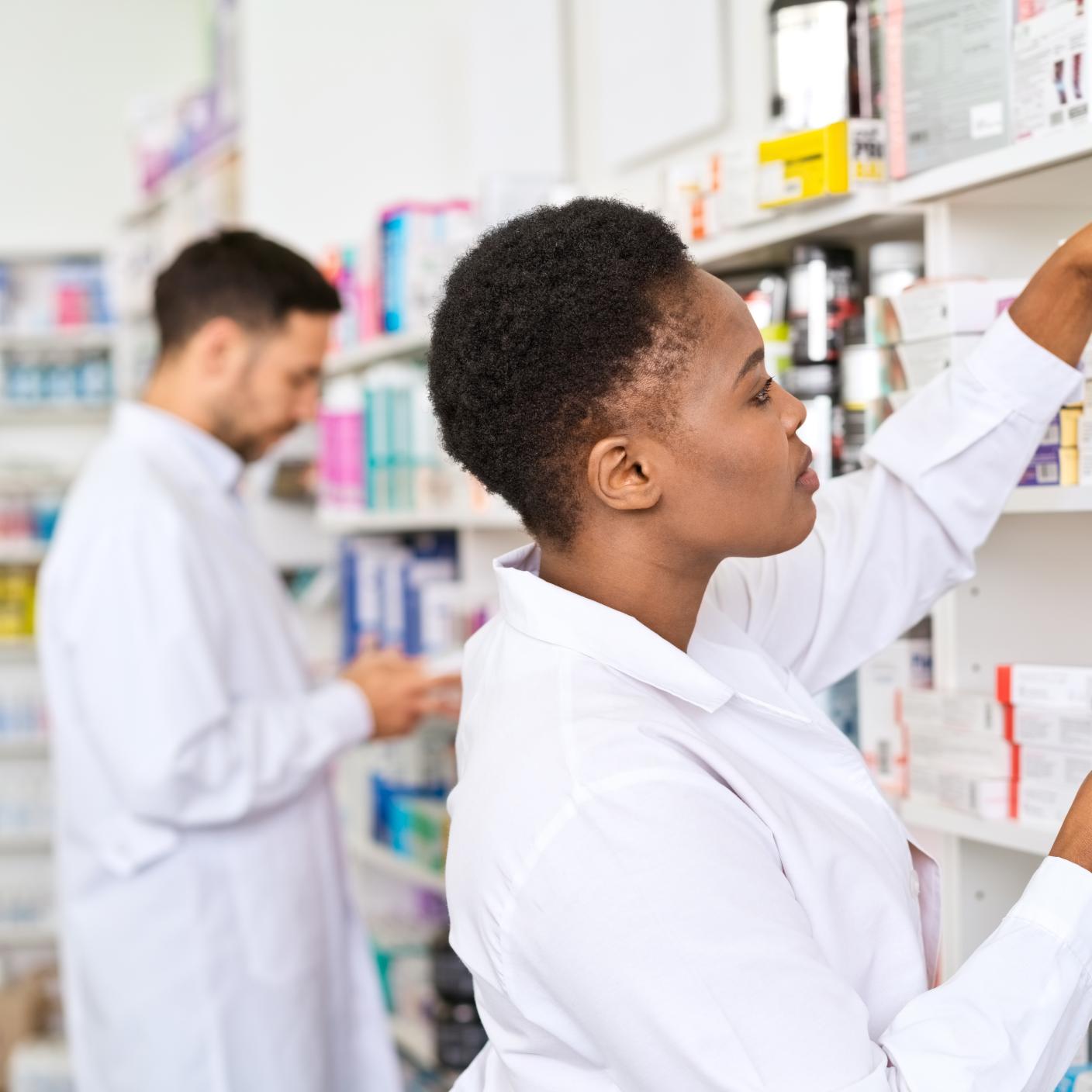 Female and male pharmacists standing in front of shelves in pharmacy, arranging medicine boxes.