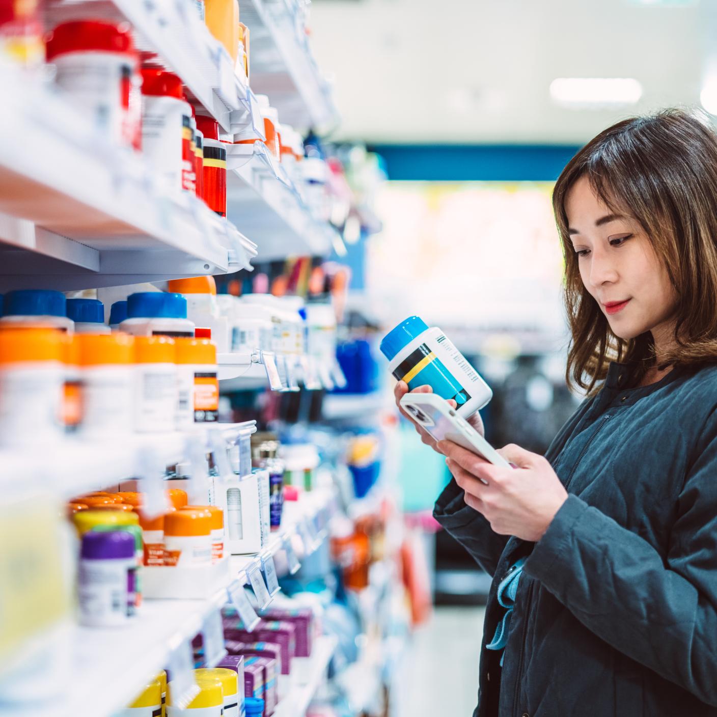 Woman searching information about the product & technology using smart phone while shopping for multi vitamin & health supplements in sup