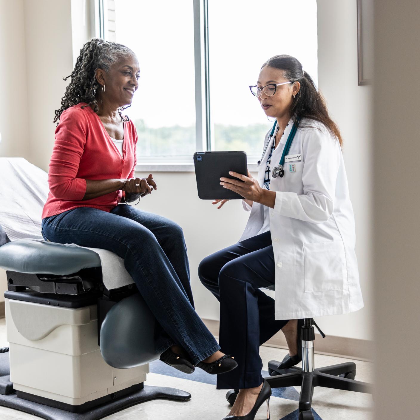 Female doctor and senior woman looking at digital tablet in exam room.