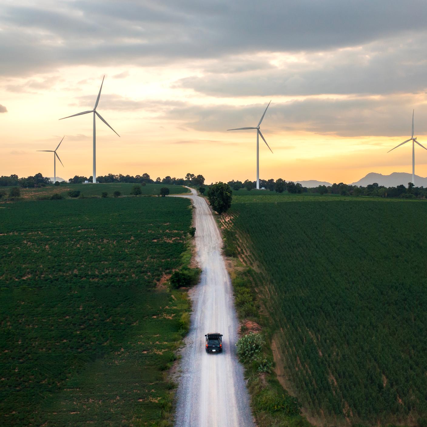Driving along a country road towards a wind farm at sunset, capturing the essence of the transition to renewable energy and a commitment to a sustainable future