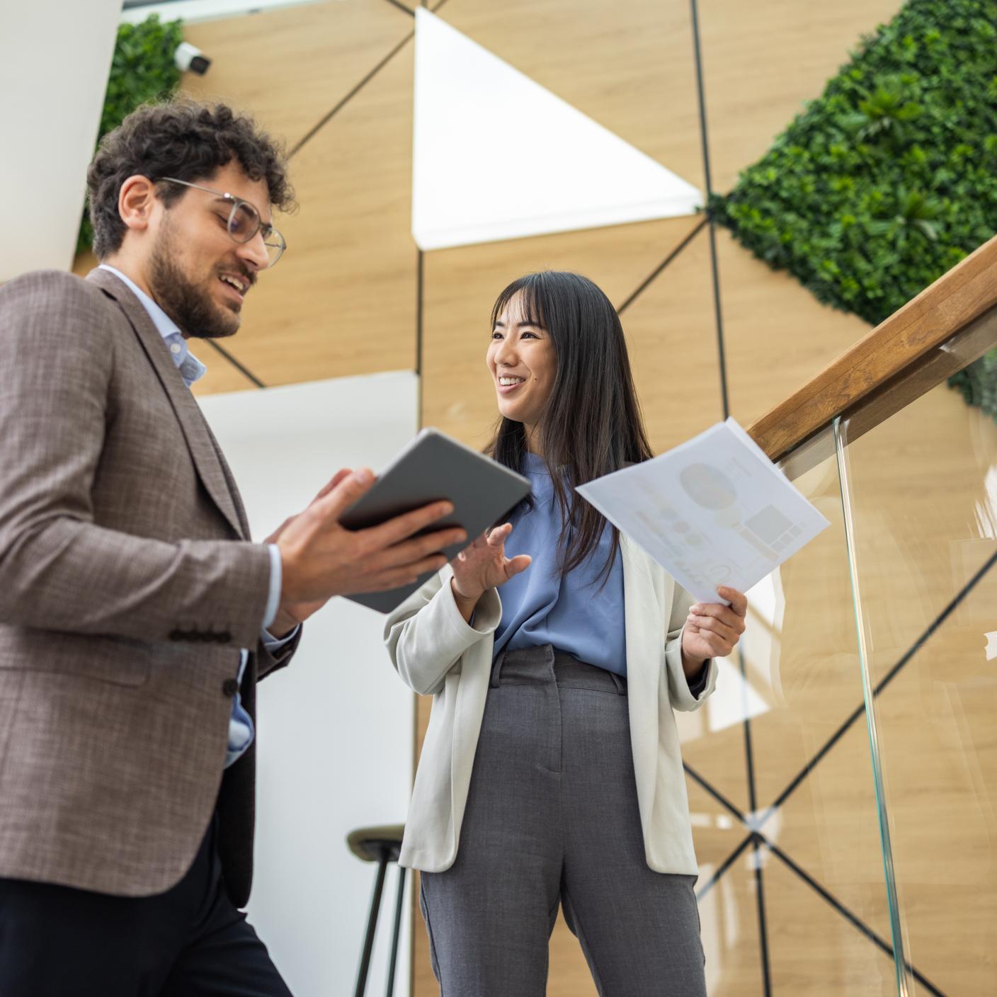 Two professionals standing together in a modern workspace, reviewing documents and discussing certification processes.