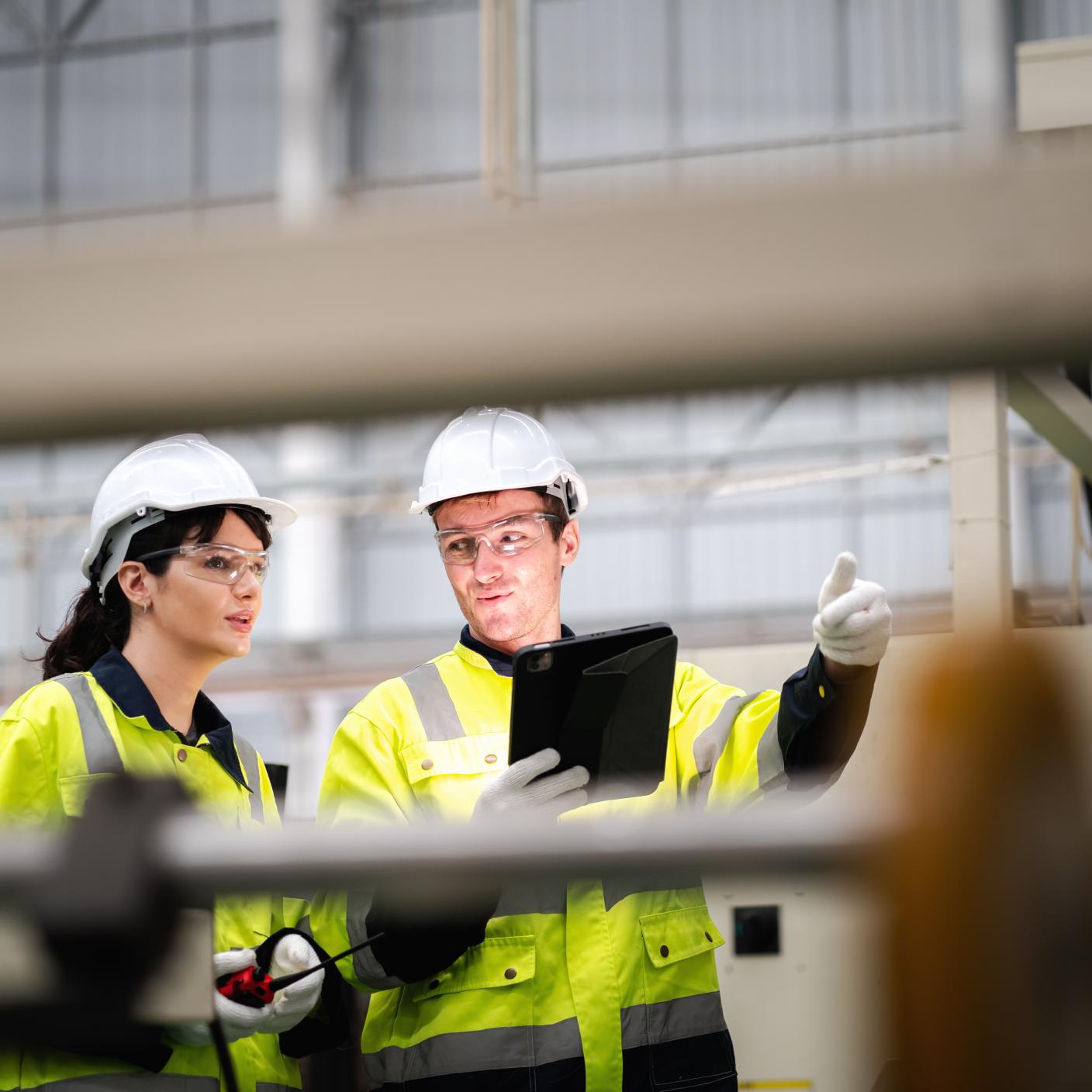 Male and female maintenance engineers in safety clothing inspect machinery in a cardboard parts factory.