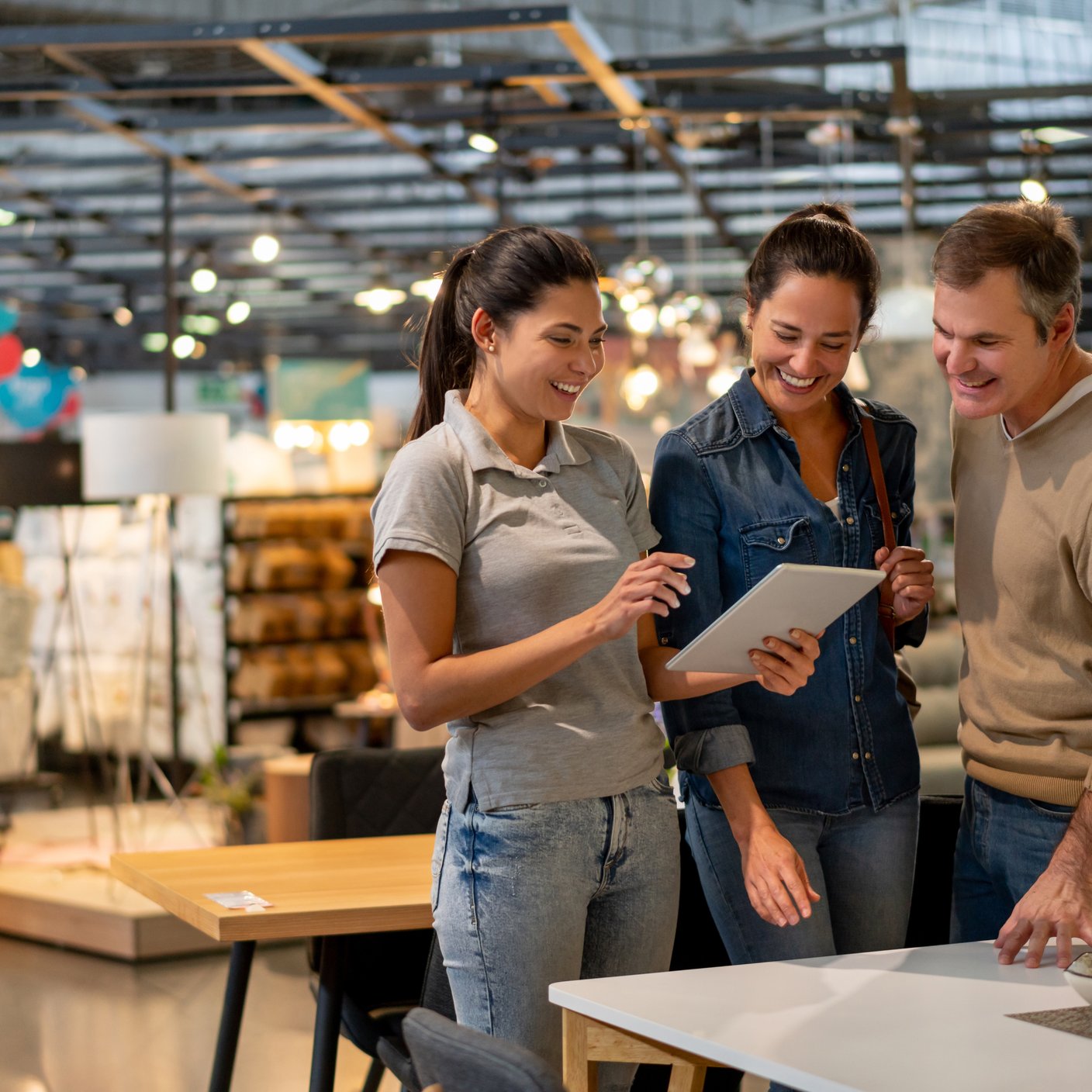 Cheerful sales woman showing a design on tablet to mid adult couple looking for furniture at a home store