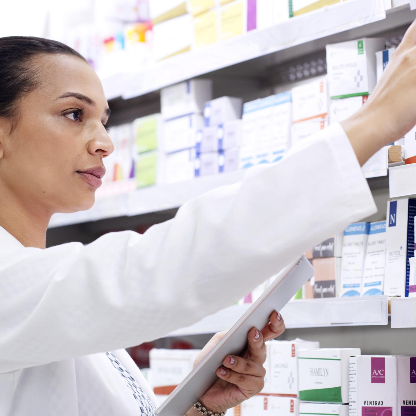 Pharmacist using digital tablet in a pharmacy while counting and sorting an inventory of retail medicine on shelves. Young woman using technology to stay organised while doing stocktake in a chemist