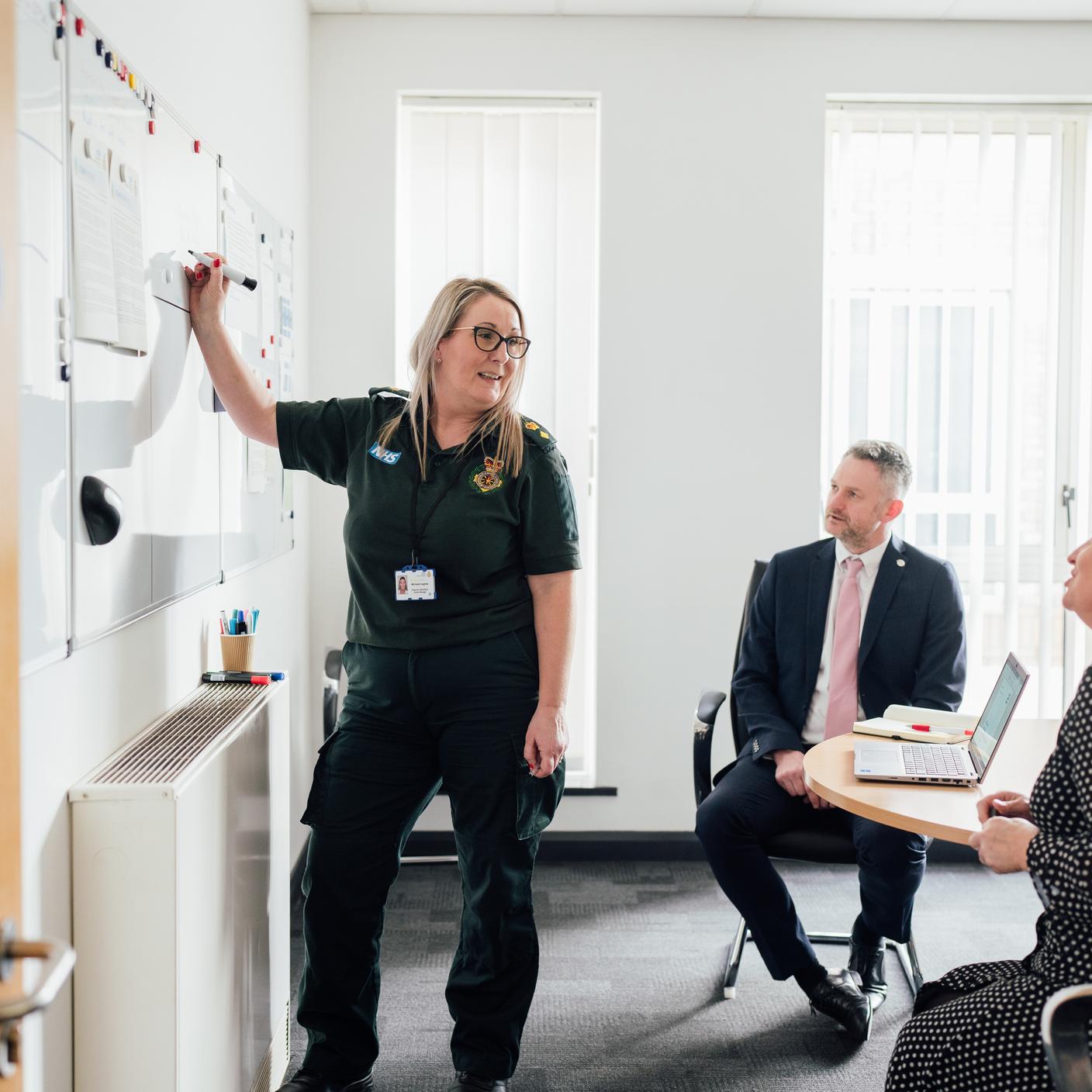 A woman writing on a board while two coworkers are listening