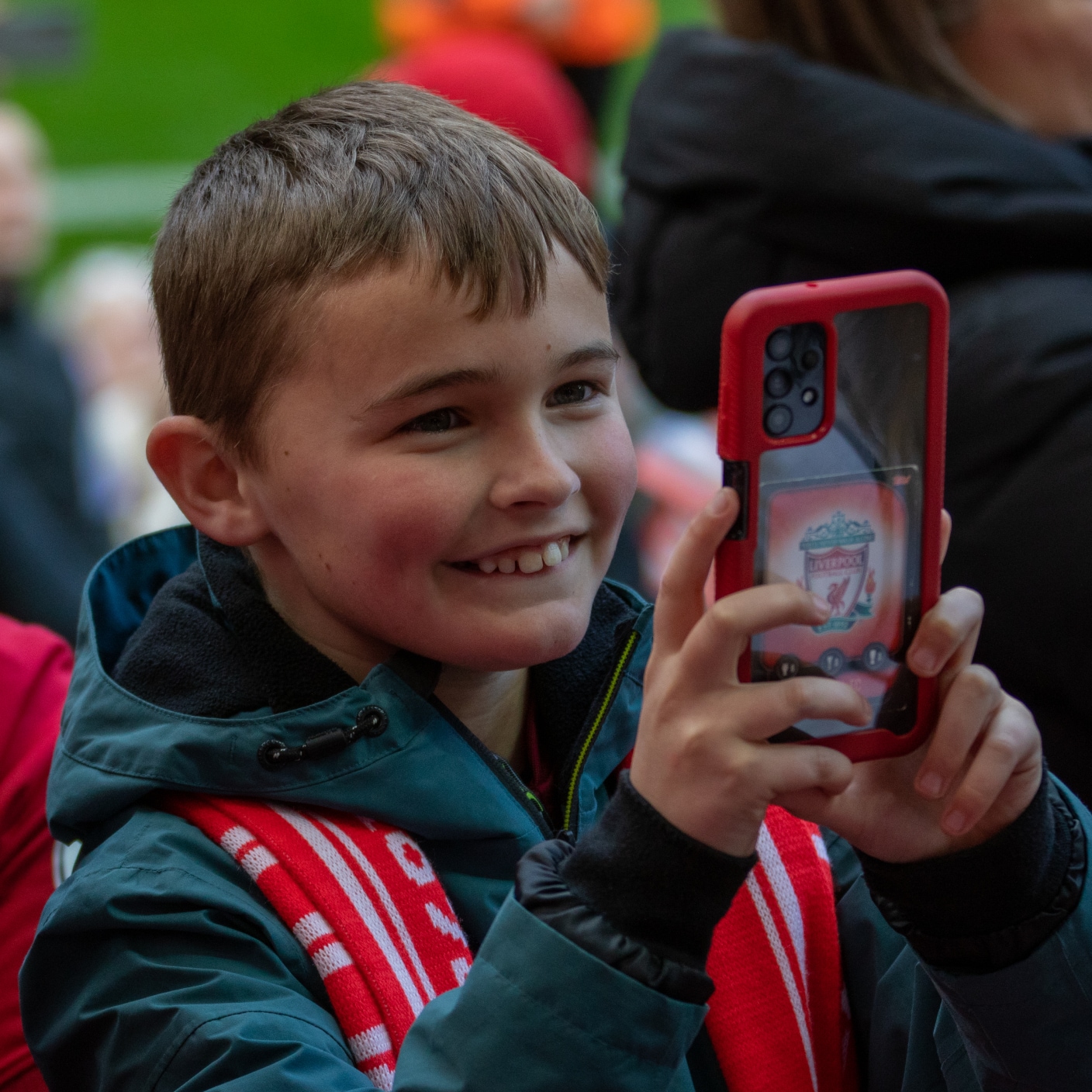 glücklicher junger Fan, der bei einem Fußballspiel sein Handy benutzt