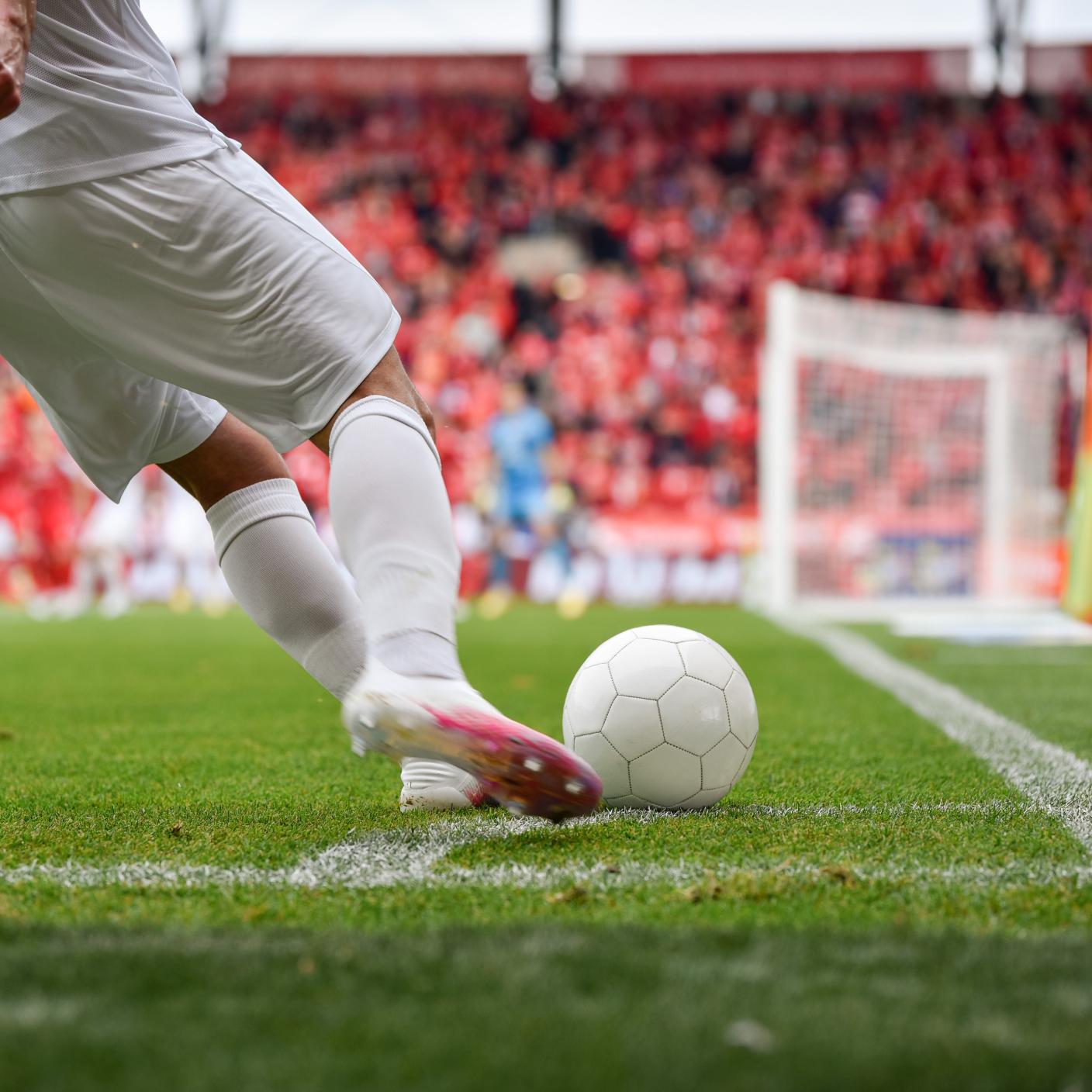 Footballer takes the corner. Detail of player's legs and the ball during soccer match.