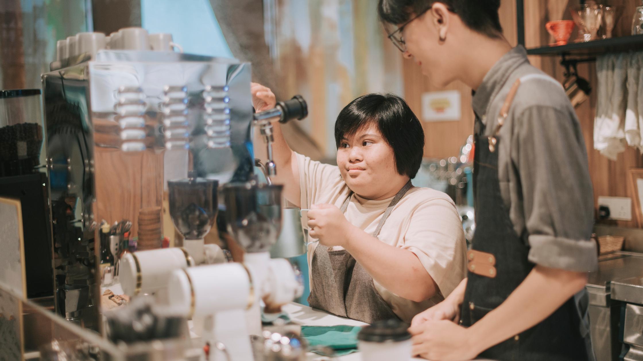 Person learning from barista making coffee in her café place of work.
