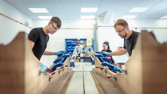 Driving business improvement - Workers on production line assembling carbon fibre parts in automotive parts factory