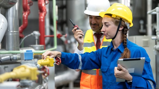 Female and male technicians inspecting work machine and equipment in industrial factory