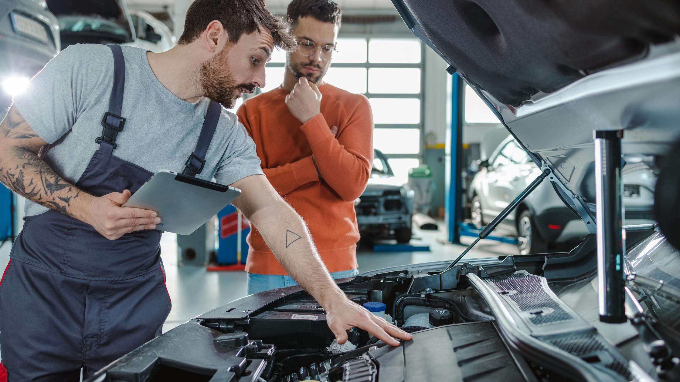 Vehicle technician pointing at engine under bonnet