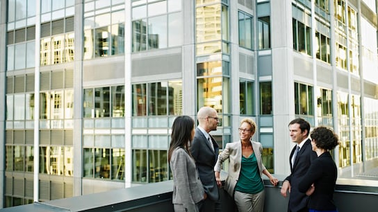 Boosting Trade and Collaboration Across the Commonwealth - Group of coworkers standing in discussion on deck of office buildings in background