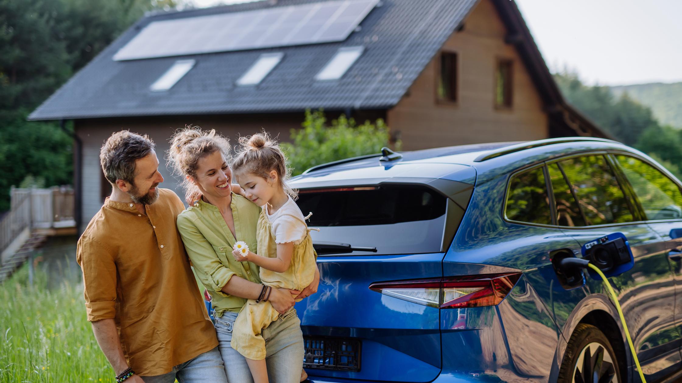 Family outside solar powered house with electric car