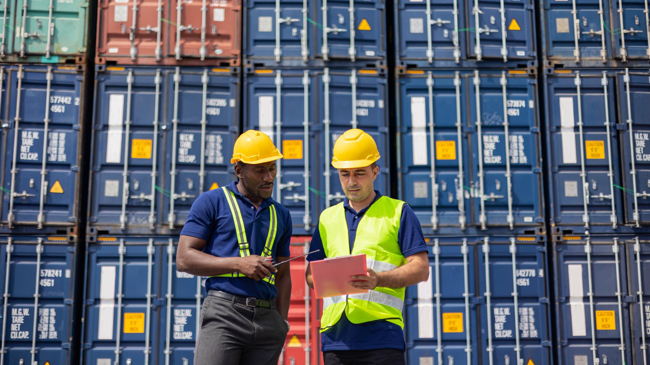 Supply Chain in Manufacturing - Two Commercial dock workers examining and confirm shipment at cargo container yard