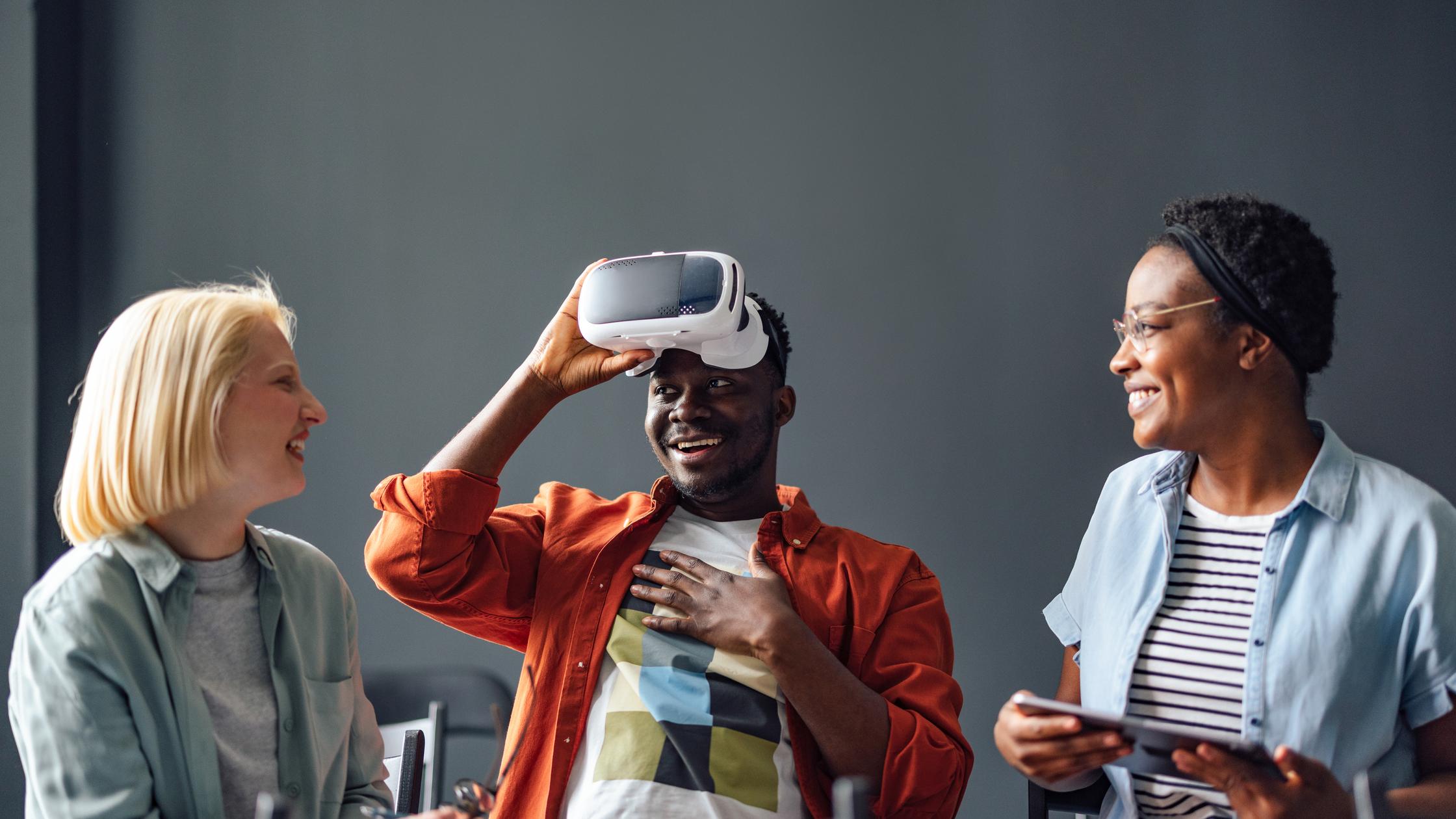 Immersive experiences - Two women smiling while their male friend is taking off virtual reality goggles