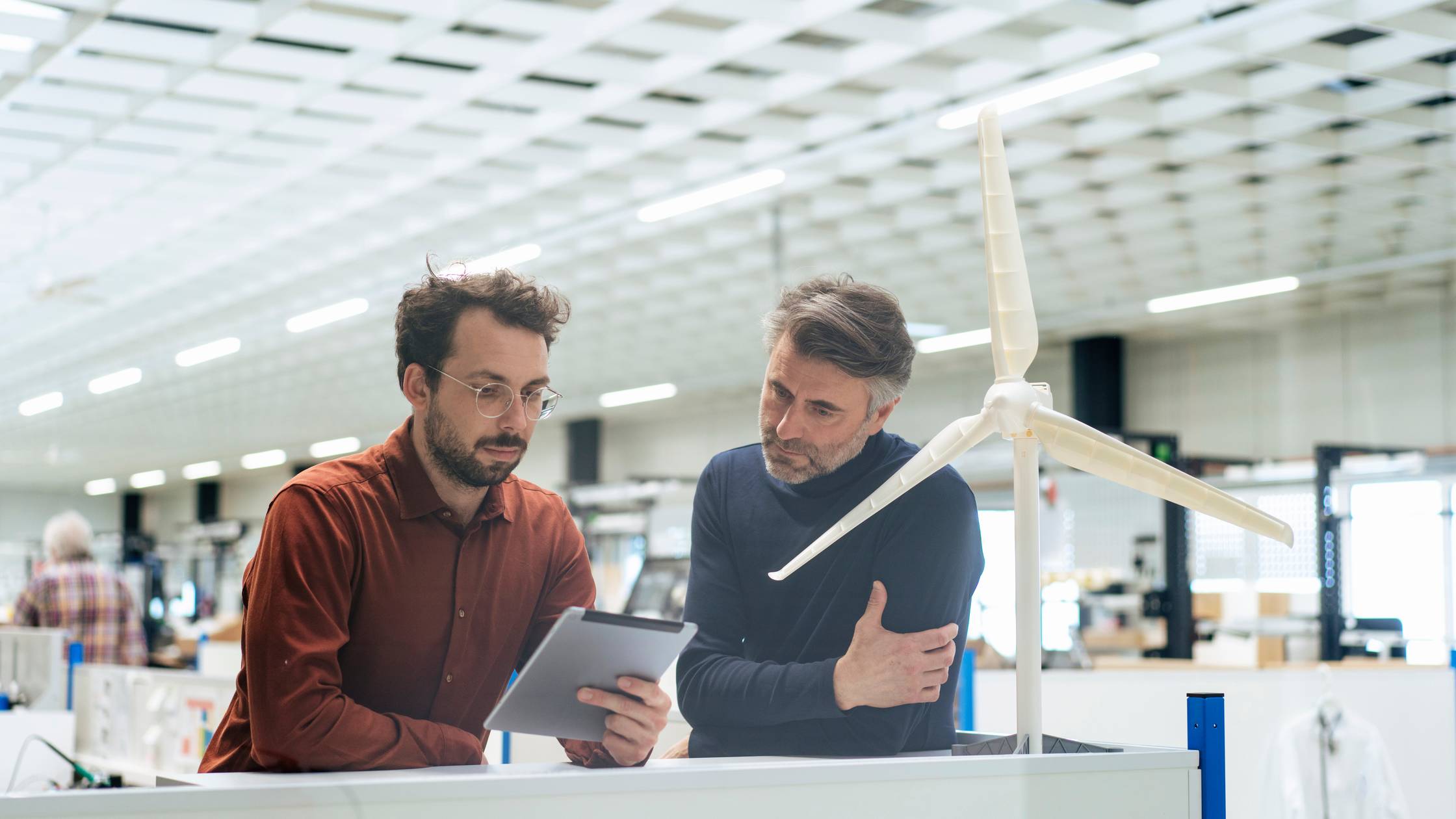 Two men looking at a digital tablet in a bright white room with turbine model in foreground