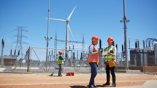 Net World 2050 - Engineers using digital tablet at sunny wind turbine power plant