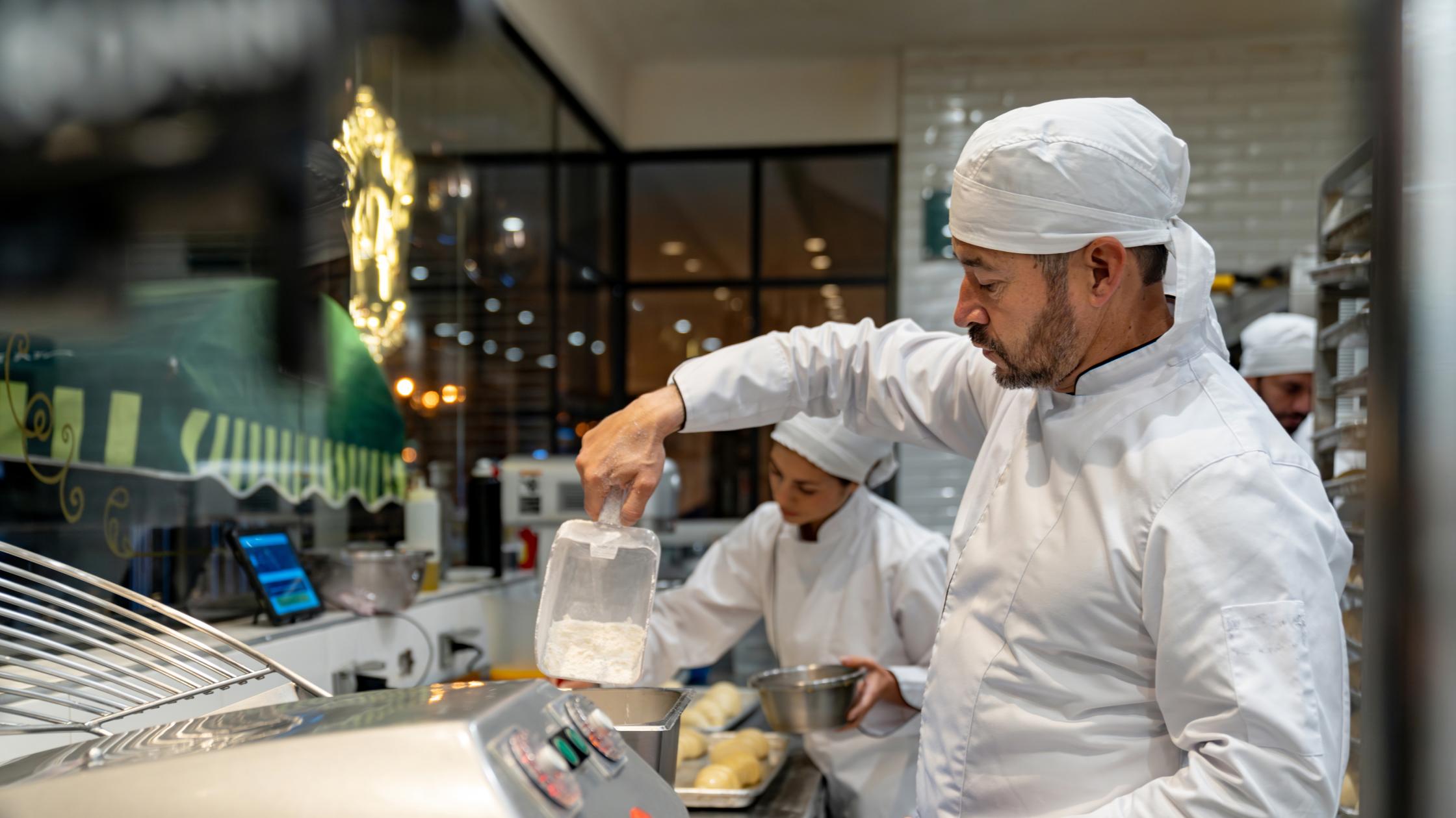 Baker making bread while working at a bakery and mixing some ingredients.
