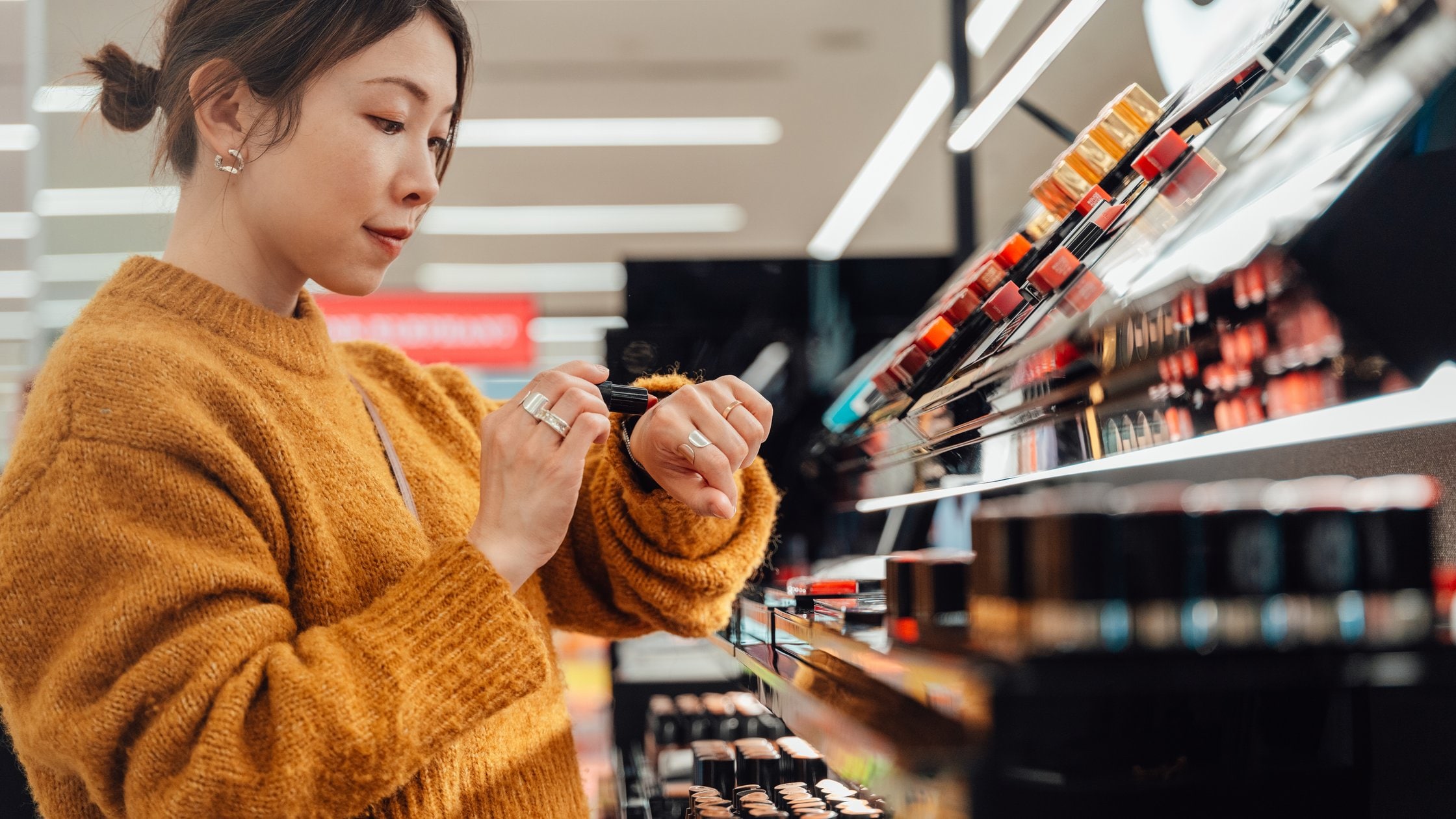 Young woman picking lipstick shades at cosmetics counter. 