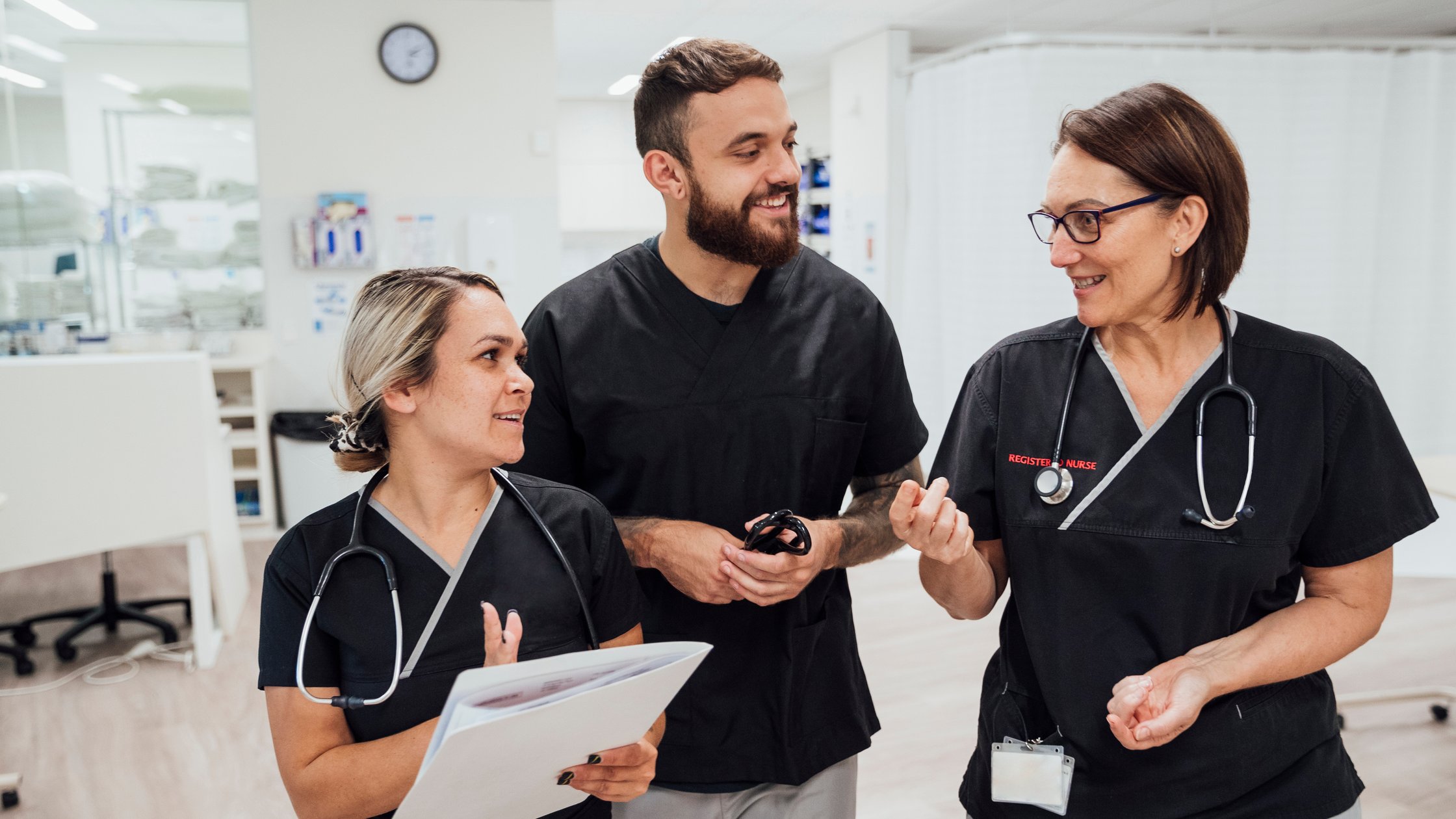 A shot of three healthcare workers walking and talking through the hospital ward.