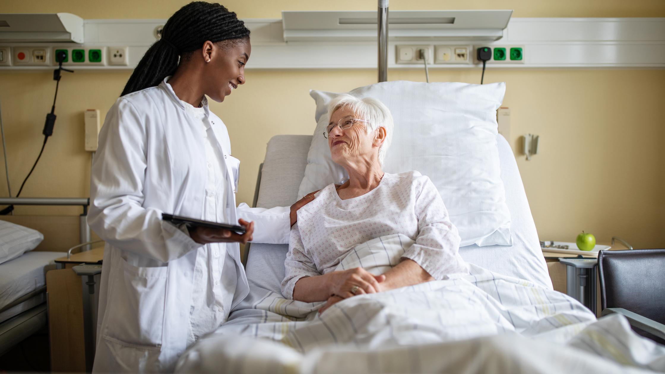 Doctor consoling senior patient during visit in ward at hospital