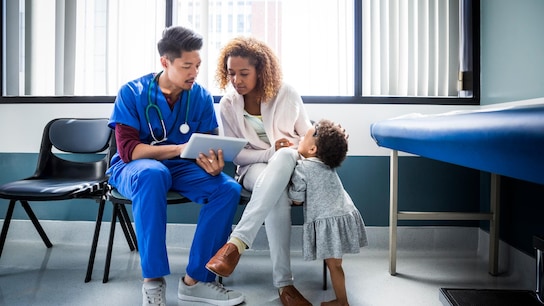 Male nurse showing digital tablet to mother by toddler in hospital
