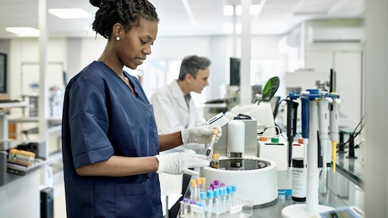 Smiling female pathology technician in blue scrubs preparing test tubes for analysis in clinical analysis laboratory.