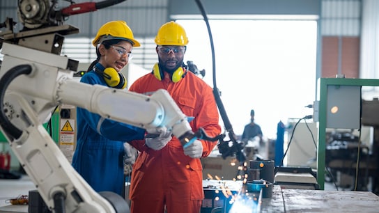 Male and female engineers analyzing the work process of industrial robotics welding to collect data to improve work processes