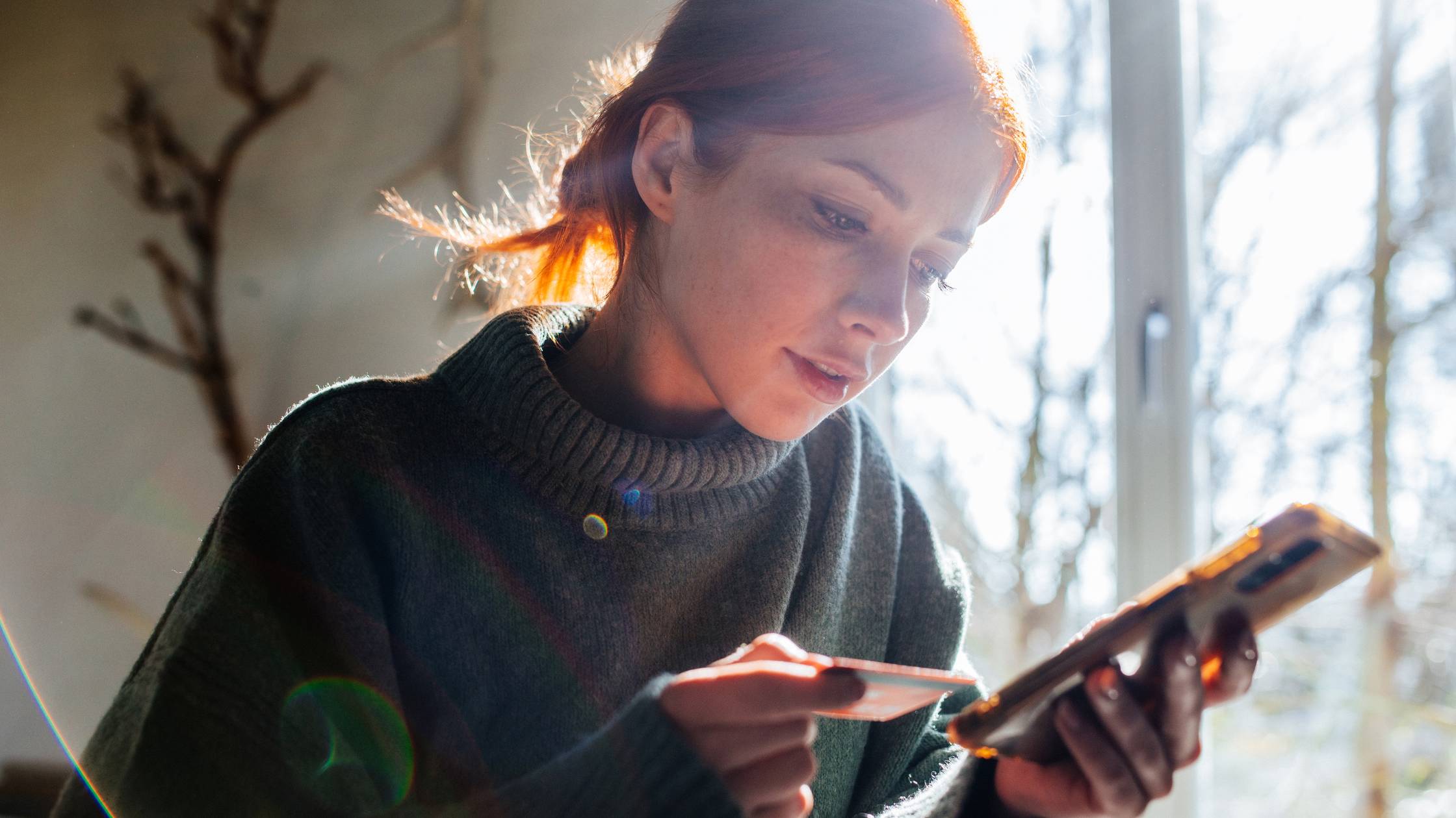 Woman shopping online with phone and credit card on hand.