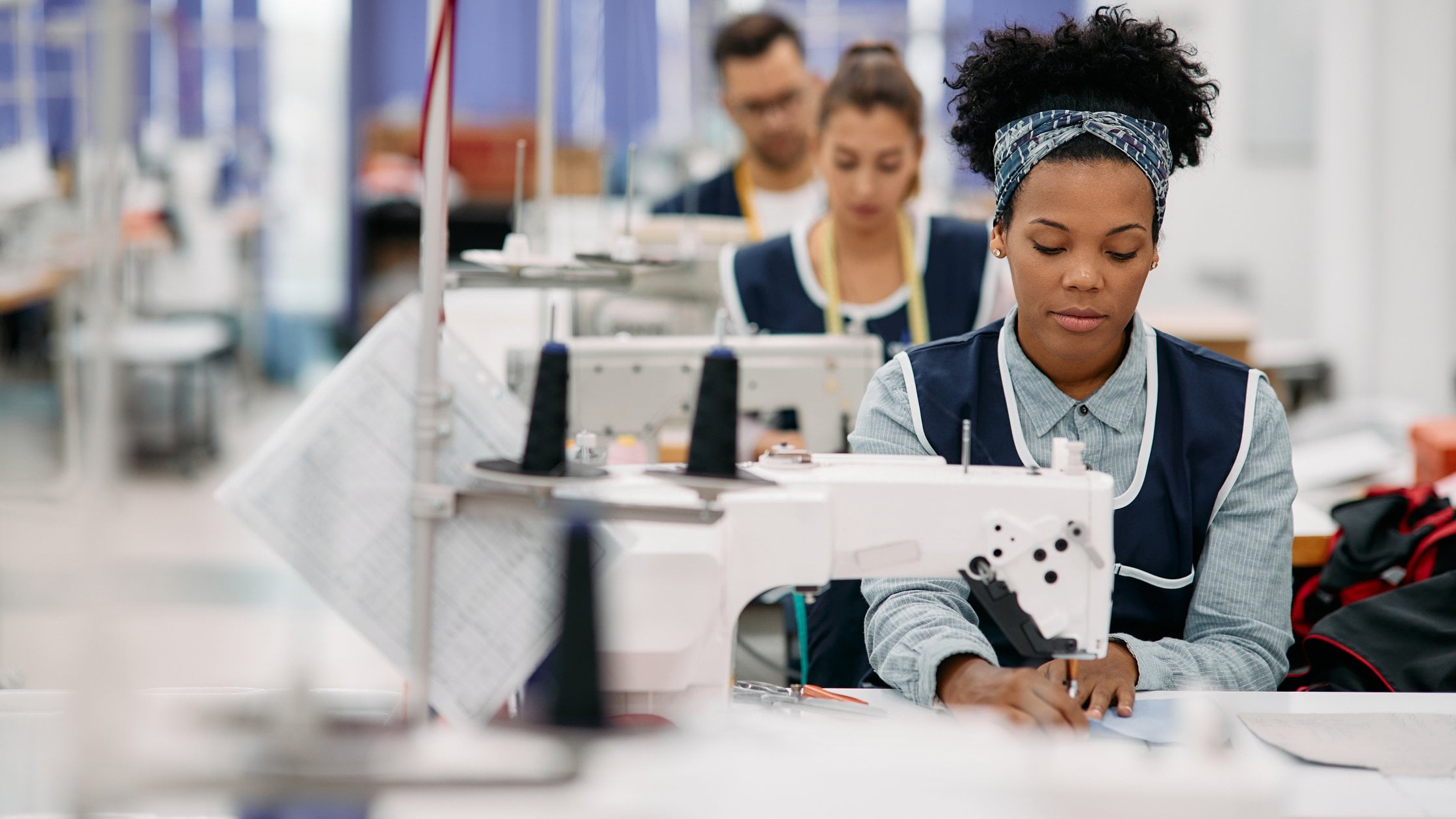 Young African American woman sewing while working as seamstress at clothing factory.