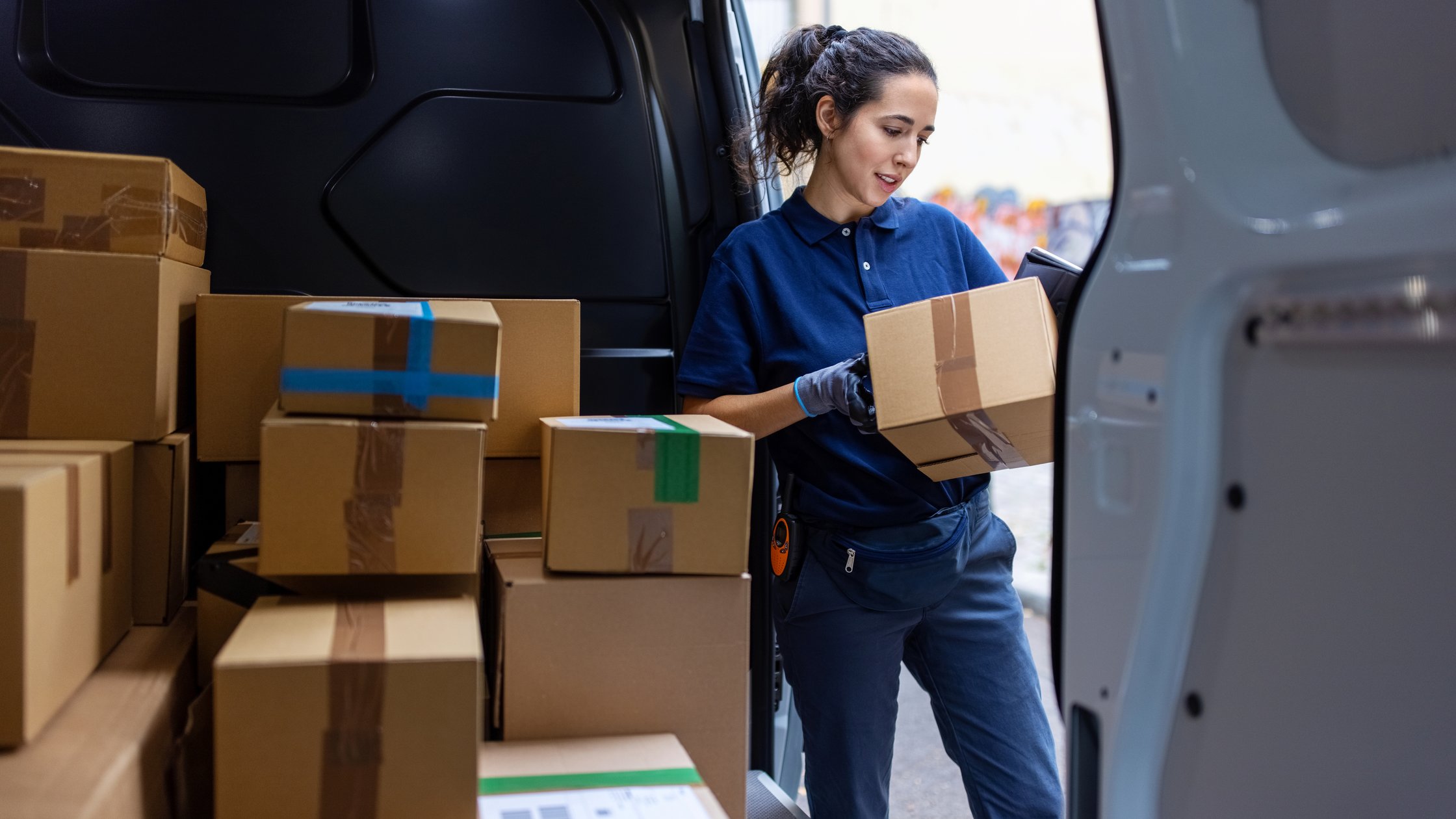 Female courier standing by shipping van checking the parcel for delivery