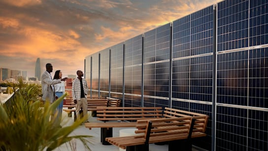 Real estate agent and couple standing on rooftop of environmentally aware office building with dramatic sky and Barcelona cityscape in background at sunset.