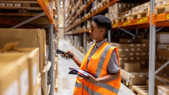 Woman working in warehouse scanning packages with bar code reader on rack