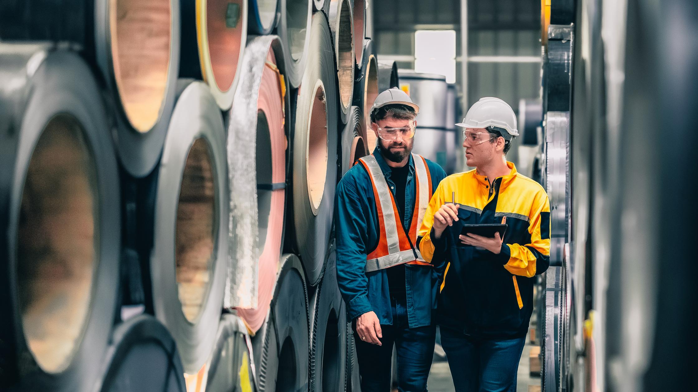 Metal sheet workers monitoring quality with precision, using digital tablets for documentation and certification, improving environmental assurance in industrial roofing and infrastructure projects.