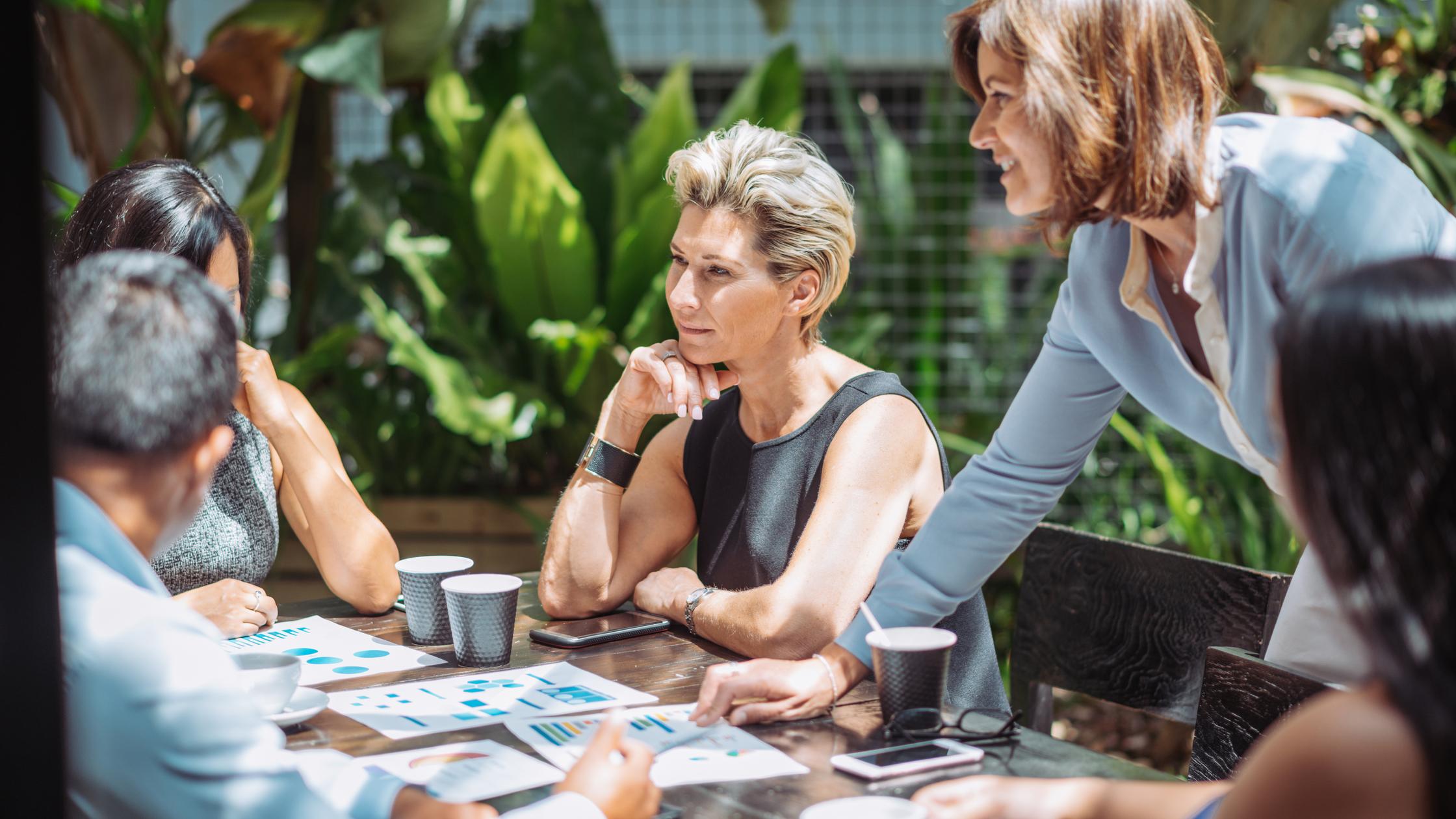 Eine Gruppe von Experten, die sich in einem Café oder Restaurant im Freien zu einem Geschäftstreffen trifft. Während sie Kaffee trinken, besprechen sie Investitionsideen und Kooperationspläne.